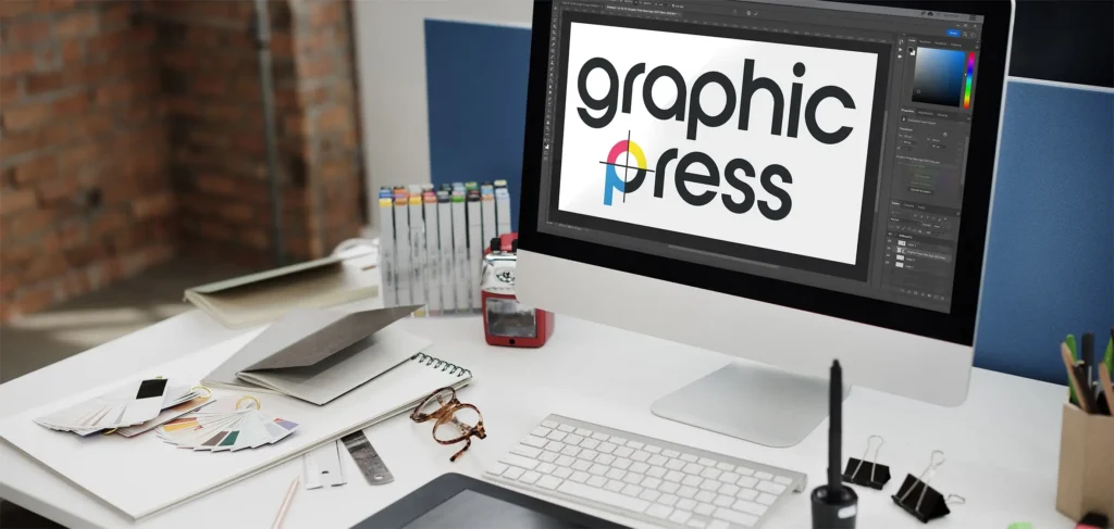 A photograph of a desk with a computer displaying the Graphic Press logo