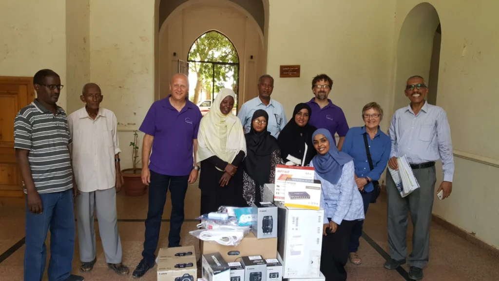 Genus staff membes with members of the Sudanese archive, positioned behind a pile of digitisation equipment
